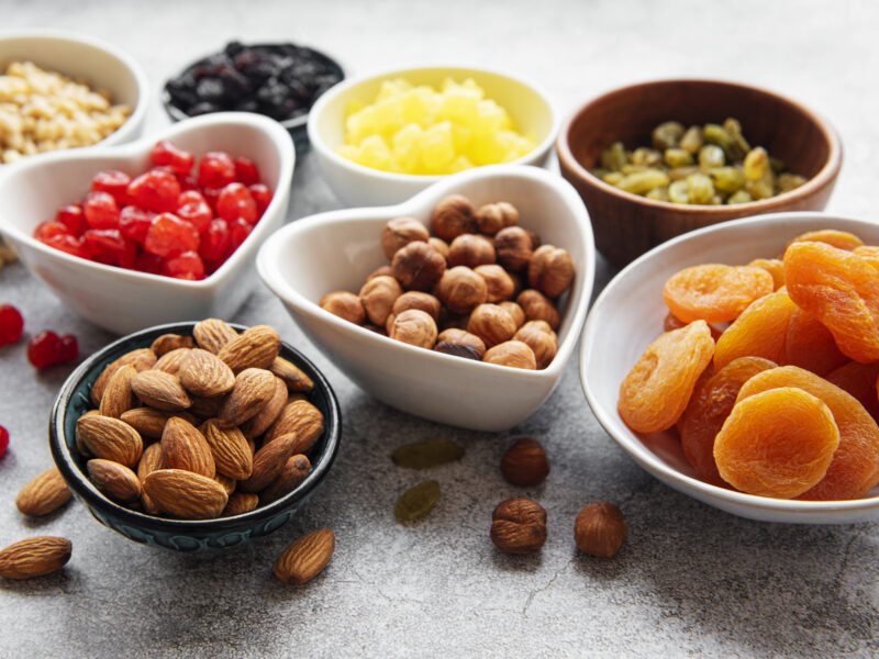 Bowls with various dried fruits and nuts on a gray concrete background