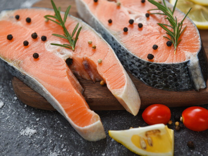 Raw salmon fish fillet and ice for cooked steak seafood / Fresh salmon steak with herbs and spices lemon rosemary tomato on wooden cutting board background